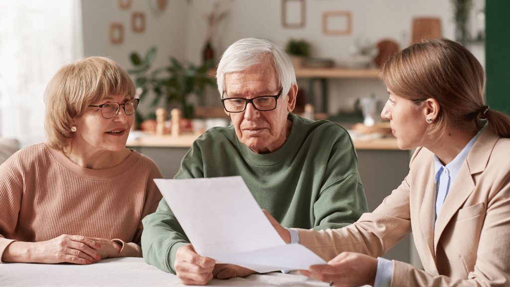 Image of an older man staring blankly at a piece of paper with his wife sitting next to him and a younger woman looking at him.